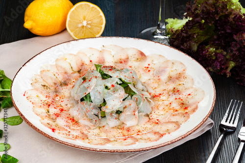 Dorado fish carpaccio served with arugula salad on white plate.