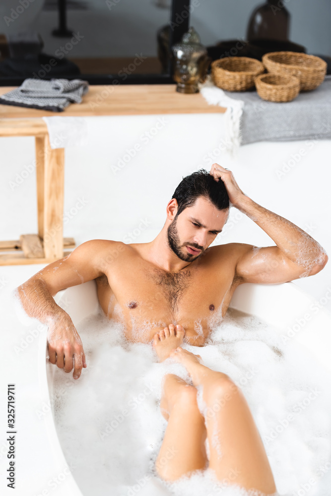 Muscular man looking away while taking bath with girlfriend at home Muscular man looking away while taking bath with girlfriend at home