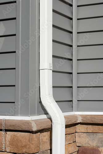 White Vinyl Downspout gutter system running along  gray horizontal sidings and Stone Cladding System on a brand new US single family home photo