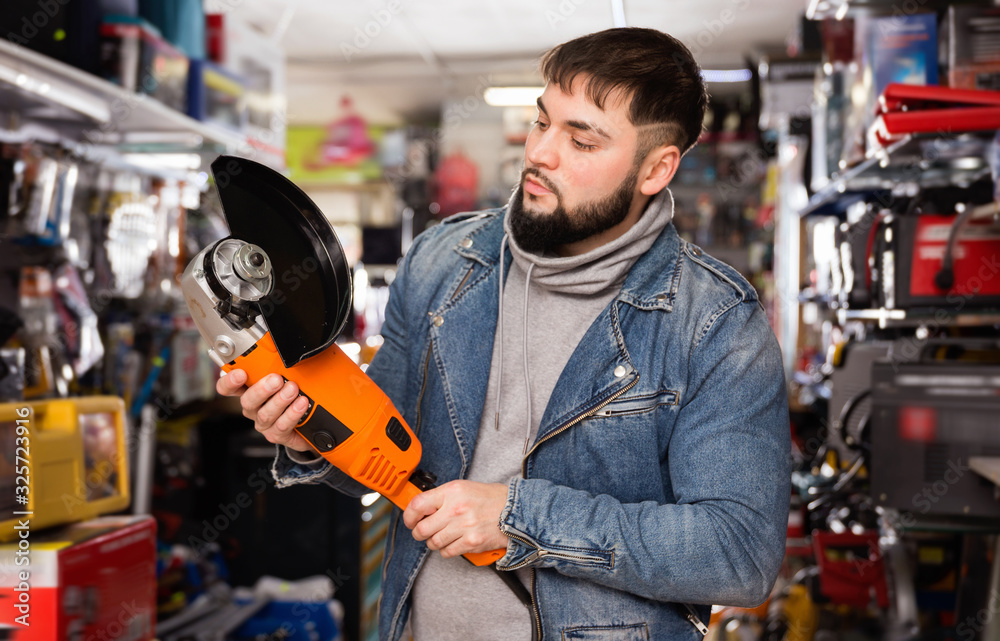 Adult bearded man is looking on new angle grinder in tools store