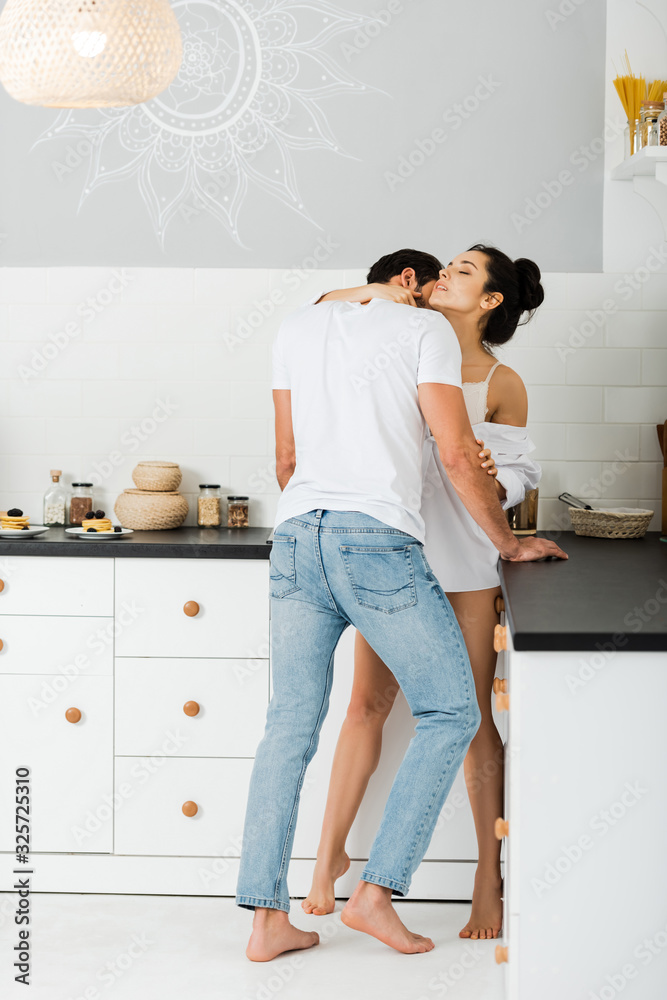 Man kissing in neck beautiful woman in bra and shirt in kitchen Man kissing in neck beautiful woman in bra and shirt in kitchen