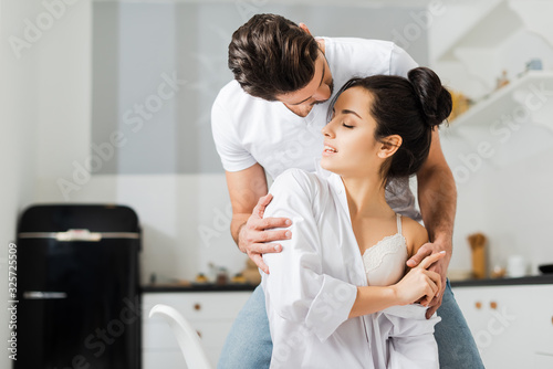 Man hugging attractive girlfriend in shirt and bra in kitchen