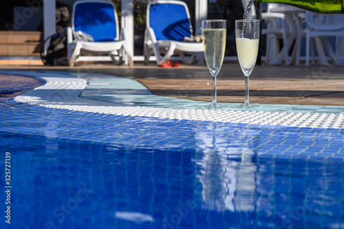 Pool party with two glasses with bubbles white champagne or cava wine, romantic event or all inclusive holidays