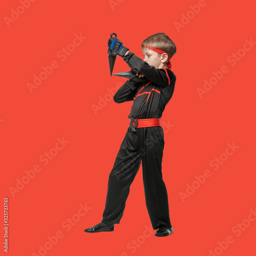 Full photo of ninja boy in kimono ready to throw knife on red background