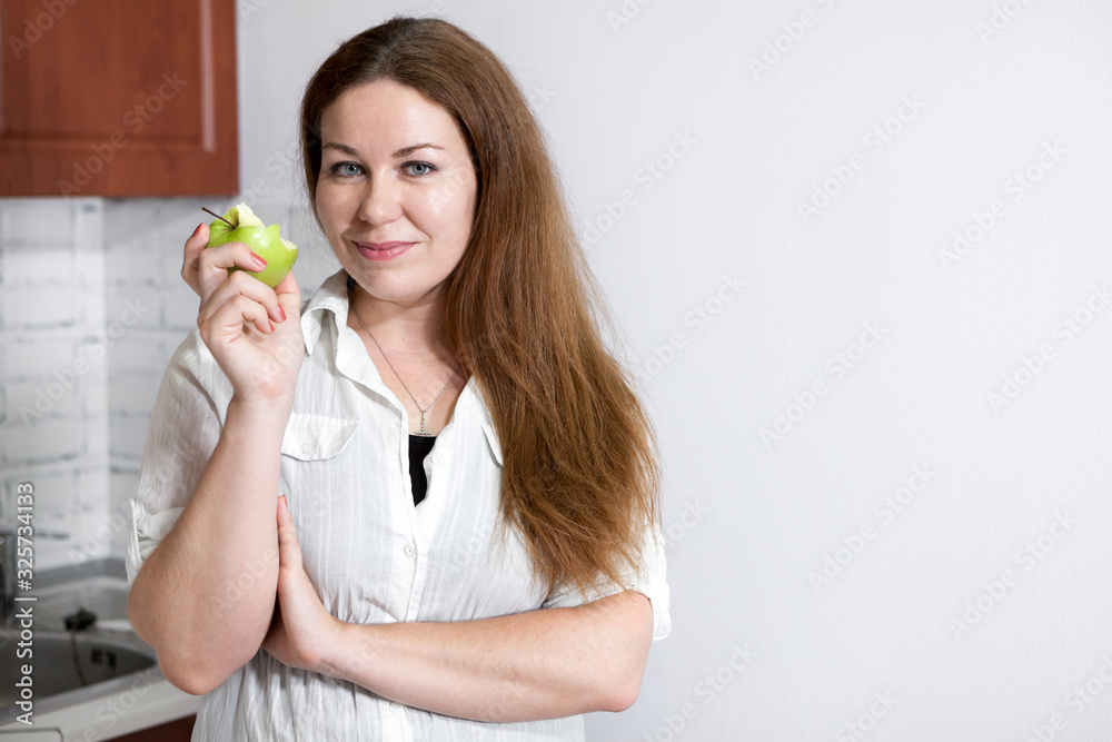 Woman eating green tasty apple while standing in the kitchen, copy space on wall Woman eating green tasty apple while standing in the kitchen, copy space on wall