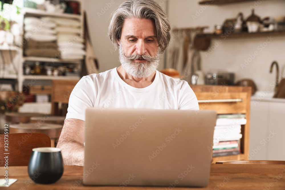 Image of serious mature man working with laptop while sitting at table Image of serious mature man working with laptop while sitting at table
