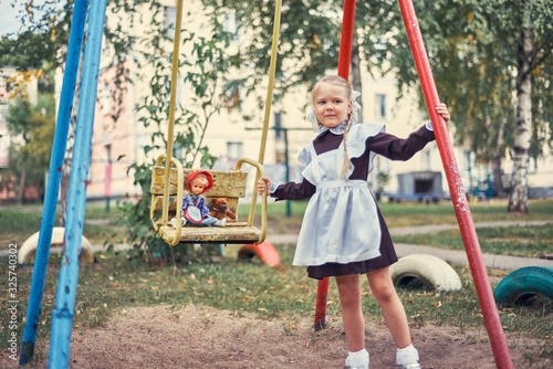 cute little girl schoolgirl in uniform rides children's toys on swing.