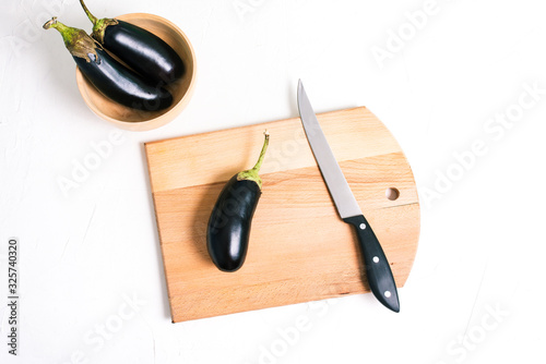 Eggplant on a white background. Fresh vegetables for cooking lunch or dinner. White table with a wooden board and knife. Healthy and diet food.