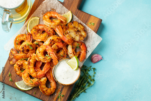 Grilled shrimp skewers or langoustines served with lime, garlic and sauce on a light blue concrete background. Seafood and beer. Top view with copy space. Flat lay