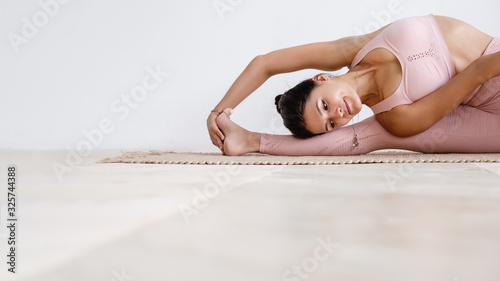Beautiful well-groomed young woman fitness instructor in a pink suit doing a warm-up stretching while sitting on a rug on the floor barefoot on a white background. Place for advertising
