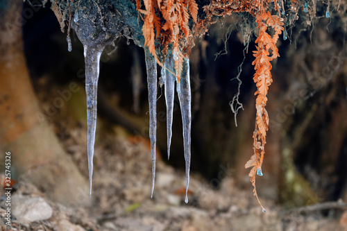 Icy little stalactite outdoors in nature on an overhang near stones.