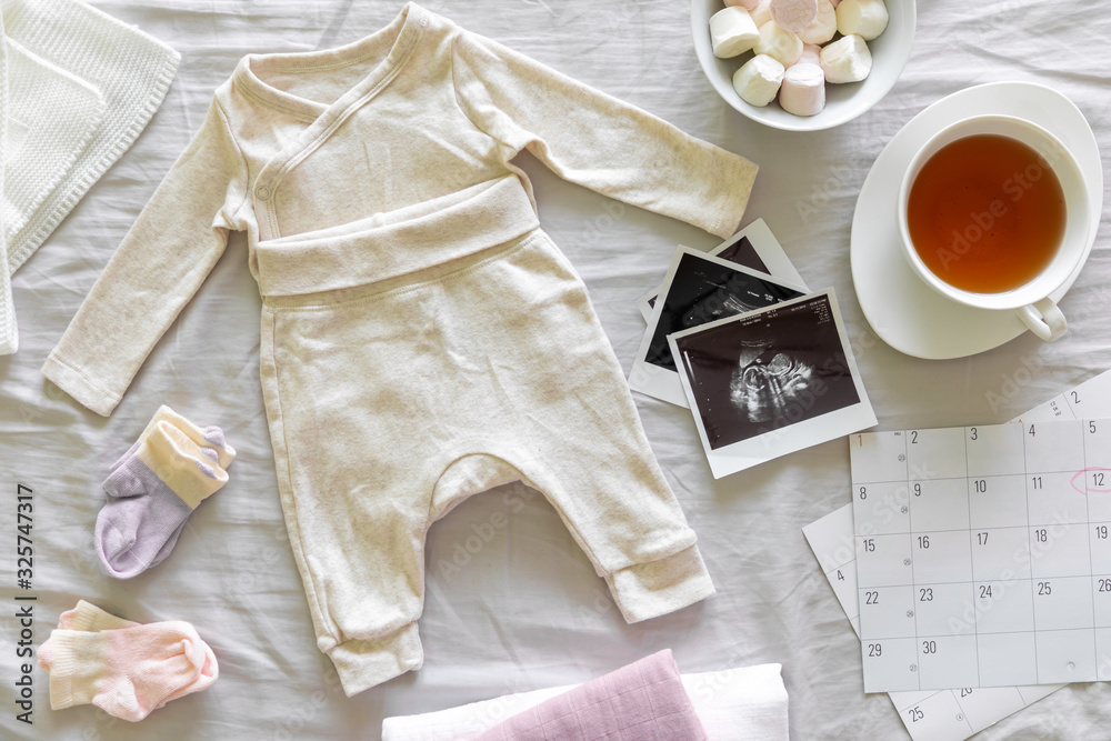 Baby clothes, calendar with the expected date of birth of baby, tea and ultrasound scan, pregnancy and birth concept Baby clothes, calendar with the expected date of birth of baby, tea and ultrasound scan, pregnancy and birth concept