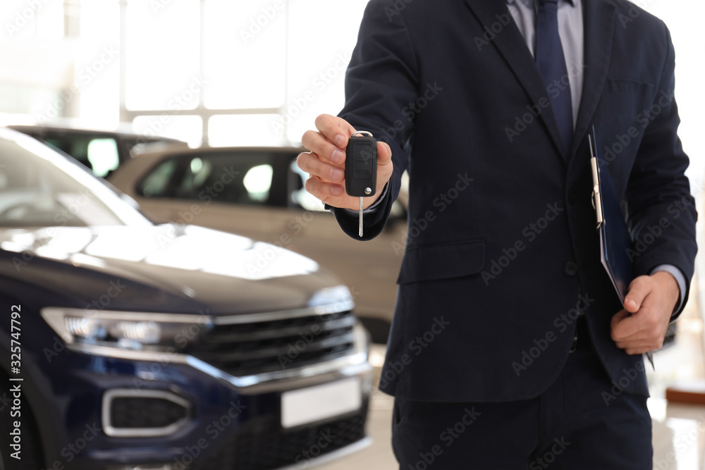 Salesman with key and clipboard in car salon, closeup Salesman with key and clipboard in car salon, closeup