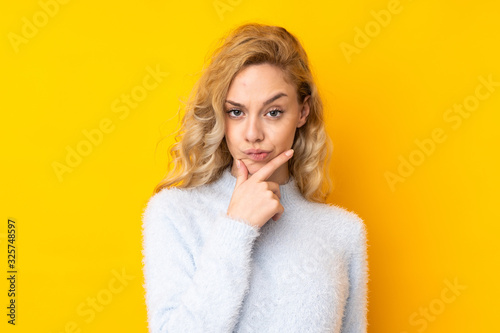 Young blonde woman isolated on yellow background thinking