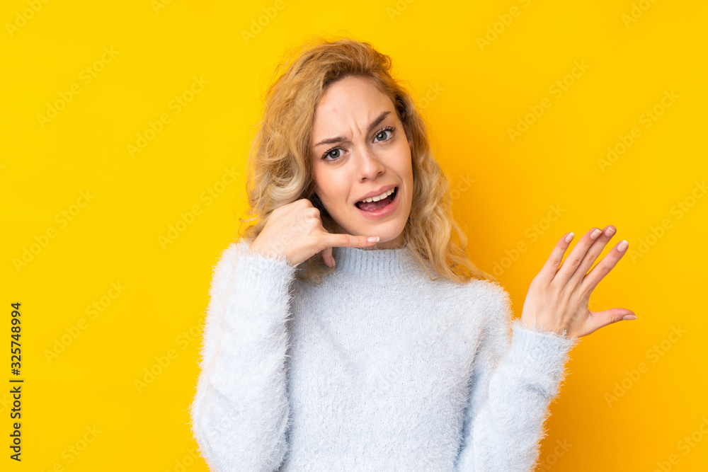 Young blonde woman isolated on yellow background making phone gesture and doubting