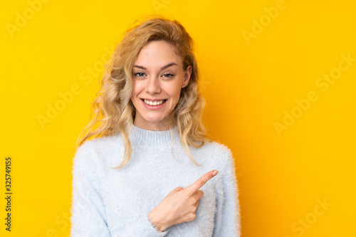 Young blonde woman isolated on yellow background pointing to the side to present a product