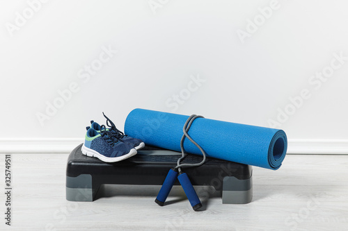 step platform, fitness mat, jump rope and sport shoes on floor at home