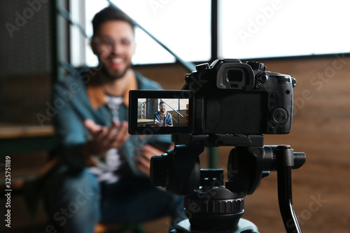 Young blogger recording video indoors, focus on camera screen photo