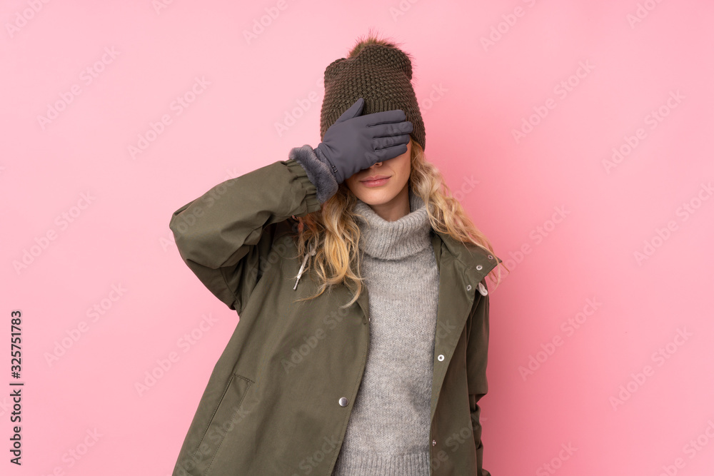 Young girl with winter hat isolated on pink background covering eyes by hands Young girl with winter hat isolated on pink background covering eyes by hands