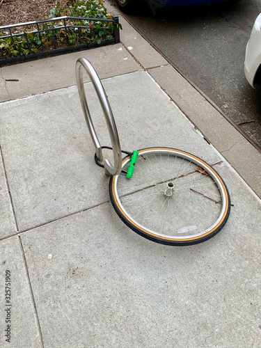 Stolen bicycle with remaining front tire locked to a bike rack. A single bicycle wheel on the street is all that is left due to stealing