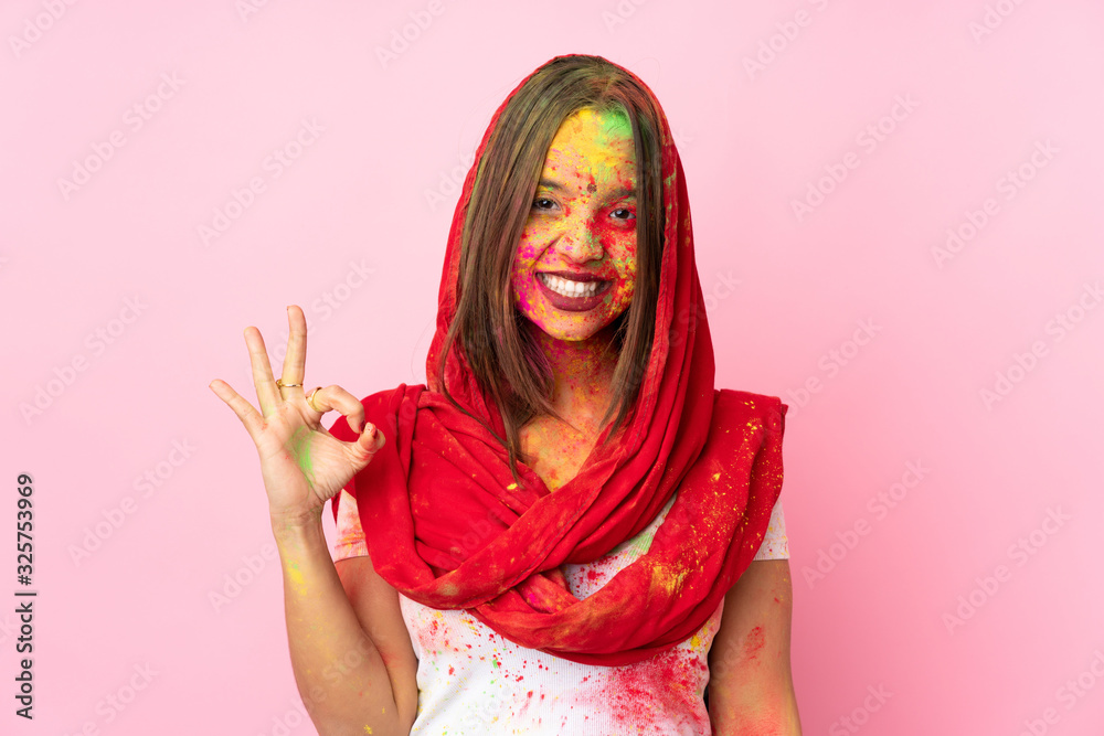 Young Indian woman with colorful holi powders on her face isolated on pink background showing ok sign with fingers Young Indian woman with colorful holi powders on her face isolated on pink background showing ok sign with fingers