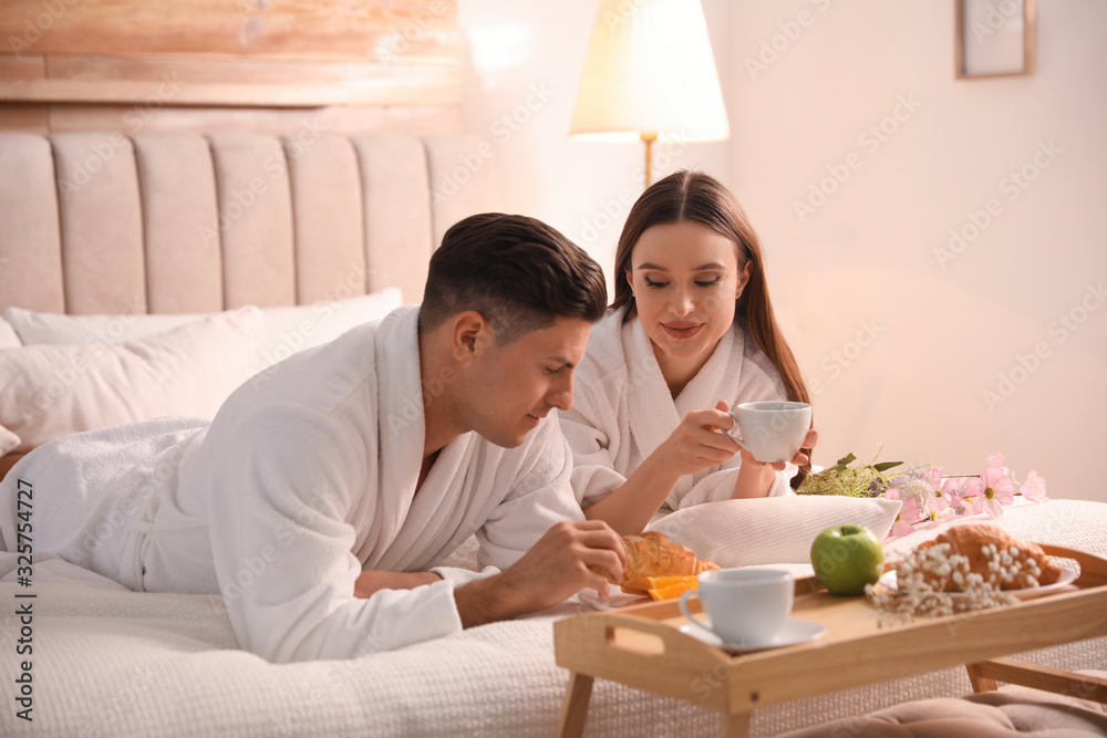 Happy couple in bathrobes having breakfast on bed at home