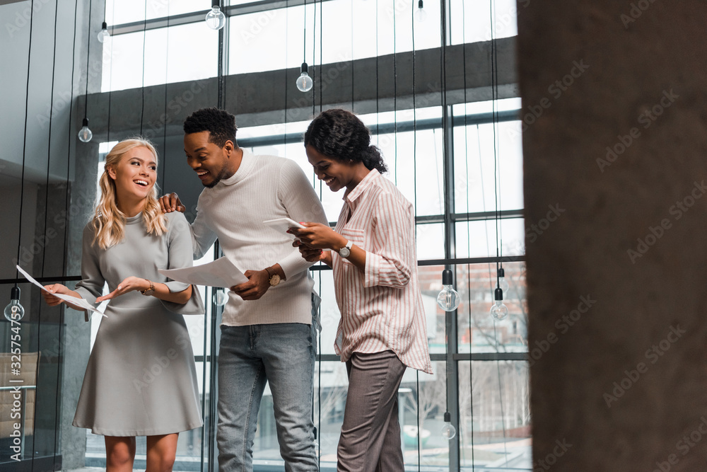 young african american businesswoman using digital tablet near multicultural colleagues holding papers young african american businesswoman using digital tablet near multicultural colleagues holding papers