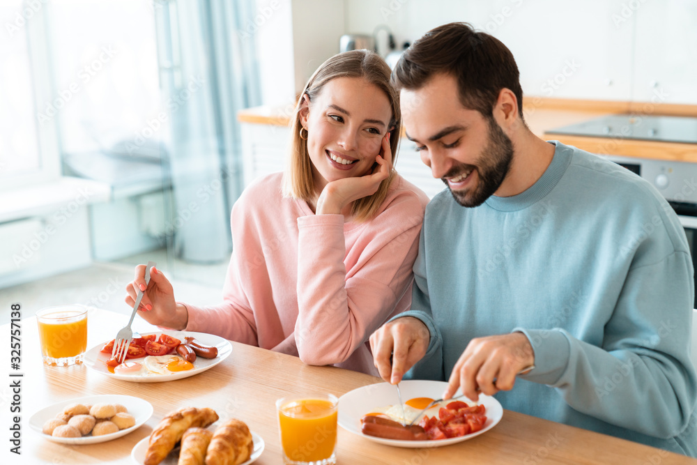 Portrait of young happy couple eating together while having breakfast
