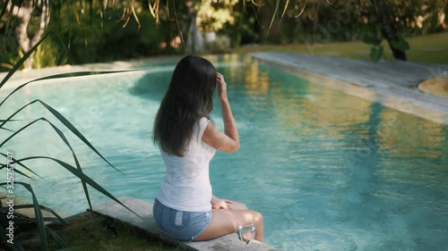 girl in t-shirt and denim shorts drinks water near pool