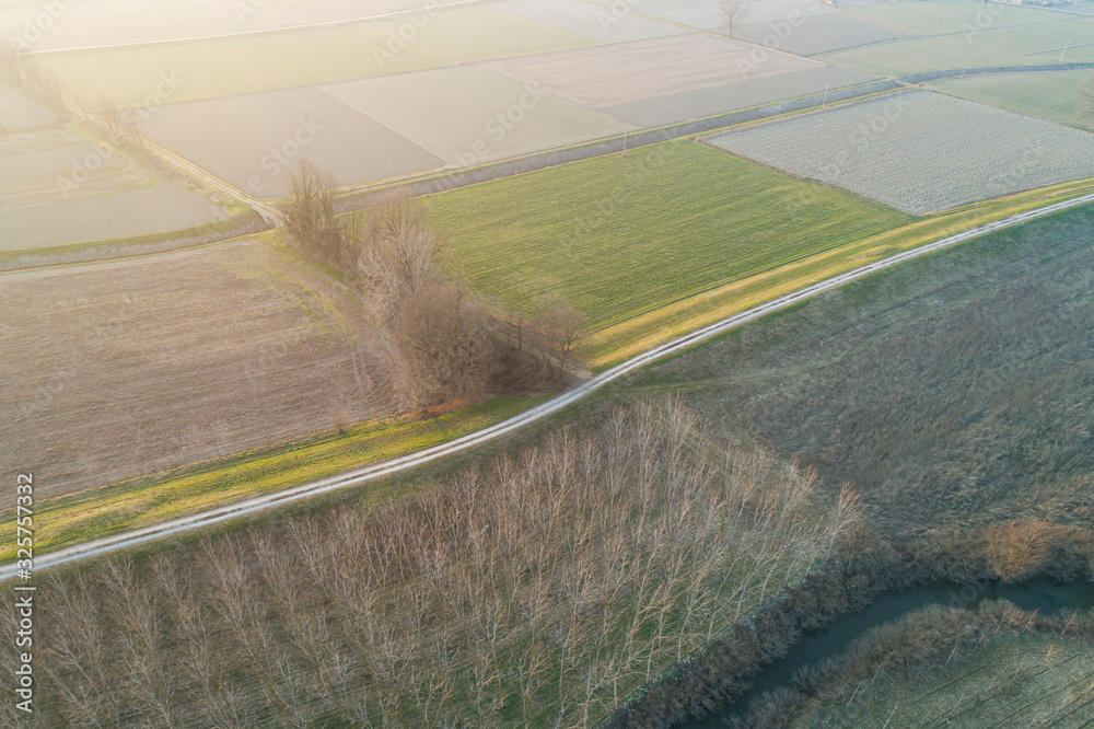 Dirt road between the fields in winter, aerial view at sunset. Landscape of the Po Valley in Italy.