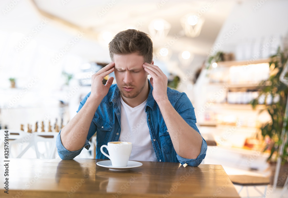 young handsome man drinks coffee during his lunch break in the cafe looks tired after haed working day, tough life concept