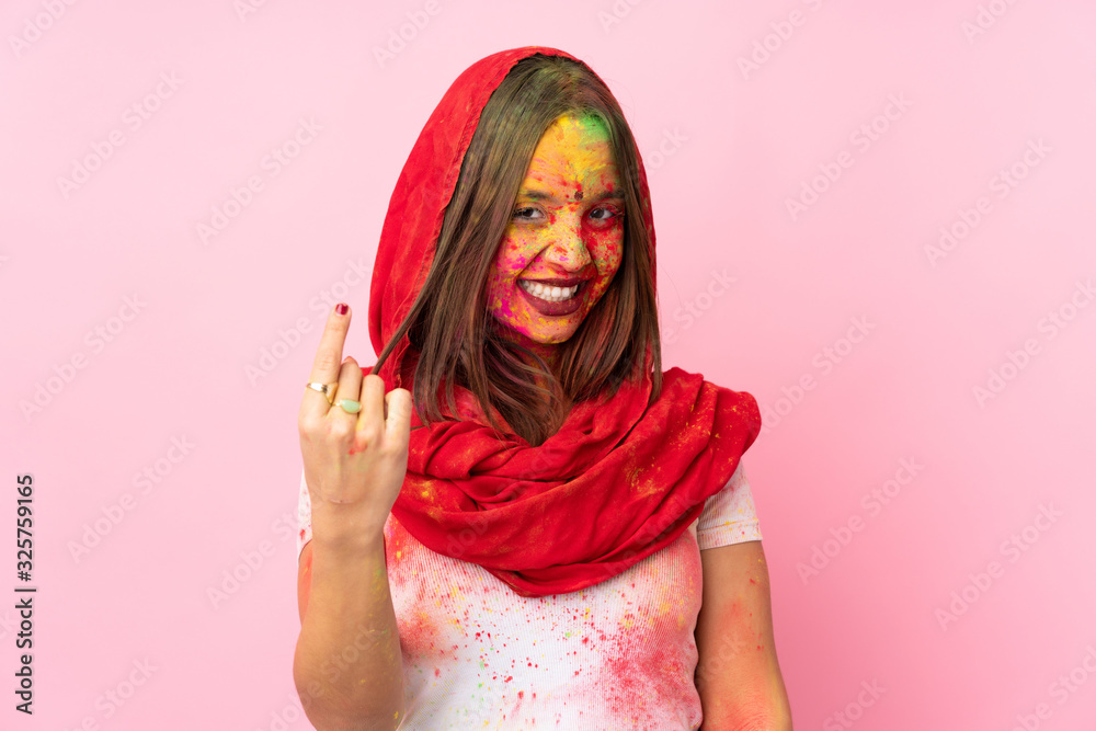 Young Indian woman with colorful holi powders on her face isolated on pink background doing coming gesture Young Indian woman with colorful holi powders on her face isolated on pink background doing coming gesture