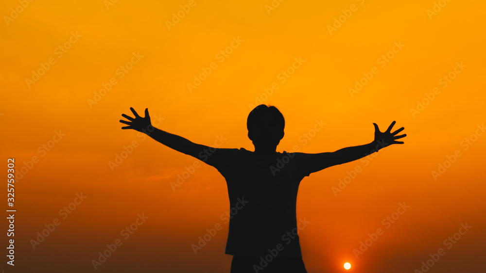 Silhouette young man with hands raised standing high up during sunset background