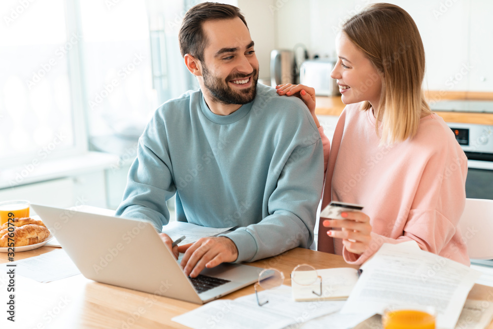Fototapeta premium Portrait of happy couple using credit card while working with laptop