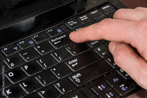 finger presses the backspace key, laptop and hand photo