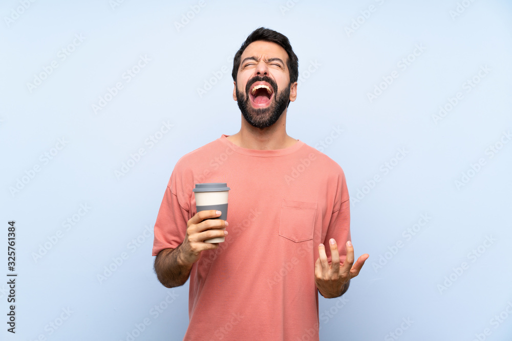Young man with beard holding a take away coffee over isolated blue background shouting to the front with mouth wide open Young man with beard holding a take away coffee over isolated blue background shouting to the front with mouth wide open