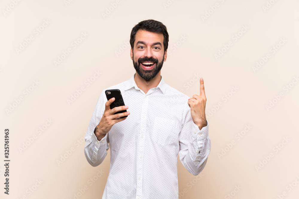 Young man with beard holding a mobile pointing up a great idea Young man with beard holding a mobile pointing up a great idea