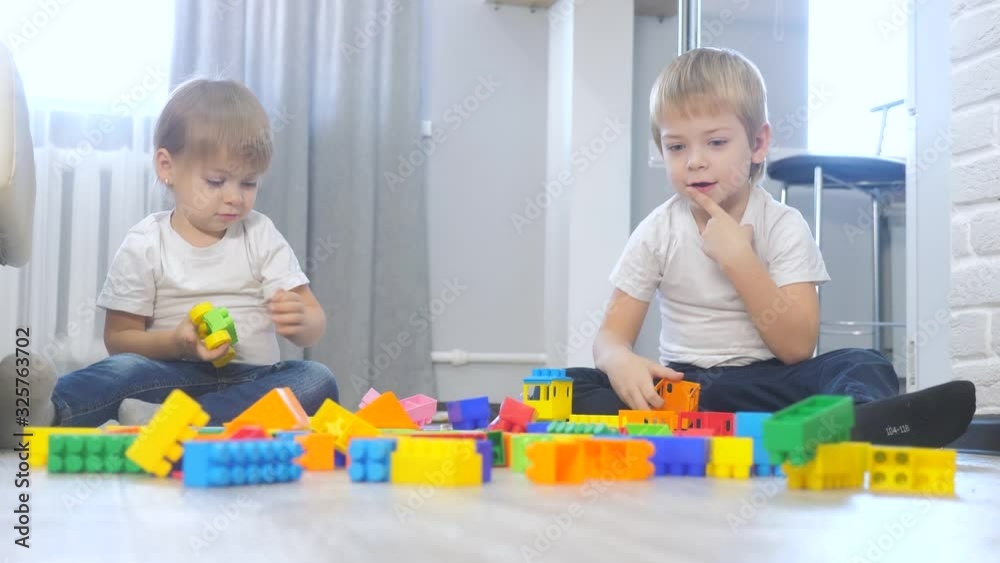 childhood happy family concept little girl collects constructor teamwork. child plays toys sitting on the floor. lifestyle children play in a team toys on the floor in the room childhood happy family concept little girl collects constructor teamwork. child plays toys sitting on the floor. lifestyle children play in a team toys on the floor in the room