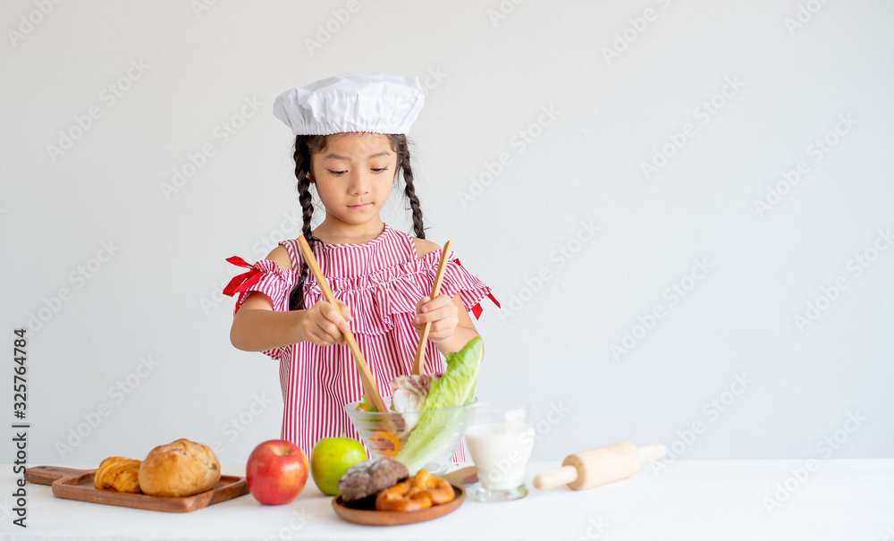 Asian little chef use wood ladle mix salad in glass bowl with white background. Asian little chef use wood ladle mix salad in glass bowl with white background.