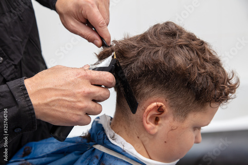 The hairdresser cuts the hair of a boy with a machine