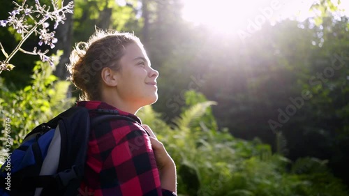 Traveller woman walking in sunny forest. Following from the back girl with backpack enjoying nature and fresh air among trees while walking through forest in bright sunshine photo