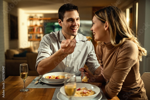 Happy man feeding his girlfriend while having dinner in dining room.