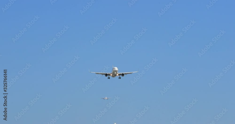 Frontal shot of modern white airplane landing, with landing gears seen released. Clear blue sky is all around the plane. Airliner smoothly descends approaching the camera and flies right above it. 4K Frontal shot of modern white airplane landing, with landing gears seen released. Clear blue sky is all around the plane. Airliner smoothly descends approaching the camera and flies right above it. 4K