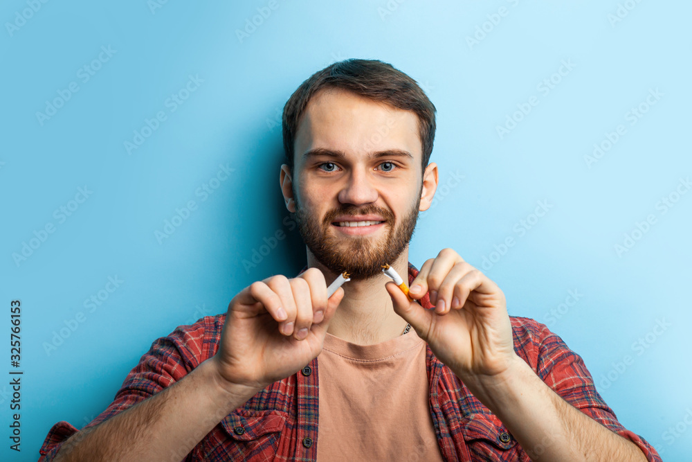 Male hand deduct cigarette. young caucasian male in red casual checkered shirt quitting from addiction. man has dark circles under eyes, going to quit smoking Male hand deduct cigarette. young caucasian male in red casual checkered shirt quitting from addiction. man has dark circles under eyes, going to quit smoking