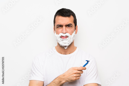 Man shaving his beard over isolated white background with sad and depressed expression