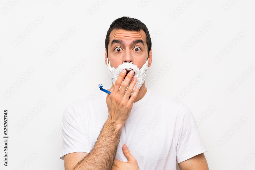 Man shaving his beard over isolated white background surprised and shocked while looking right Man shaving his beard over isolated white background surprised and shocked while looking right