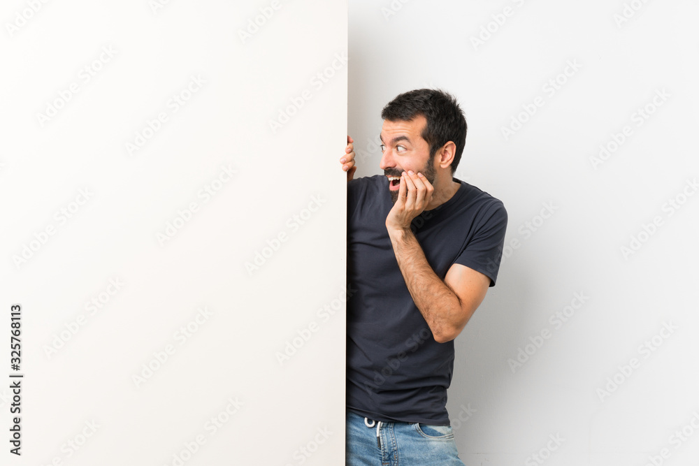 Young handsome man with beard holding a big empty placard with surprise and shocked facial expression Young handsome man with beard holding a big empty placard with surprise and shocked facial expression