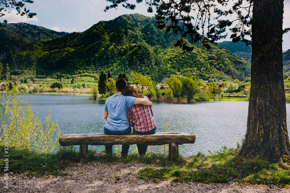 Young couple sitting on bench under a tree at lake in Italy. Young couple sitting on bench under a tree at lake in Italy.