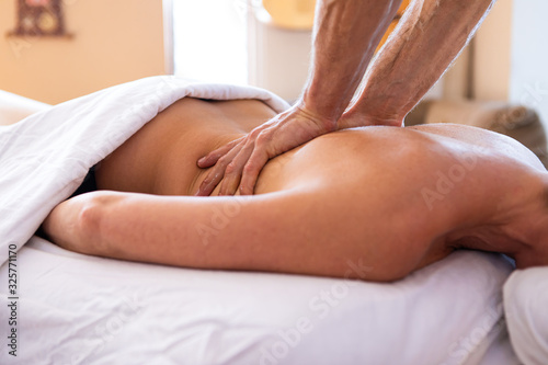 A young lady receiving Santosh massage in a cosy home environment. Spa body massage. Strong hands of professional male masseur doing gentle back massage photo