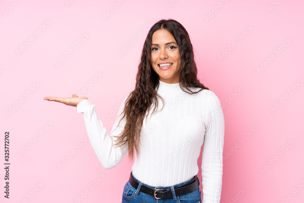 Young woman over isolated pink background holding copyspace imaginary on the palm to insert an ad
